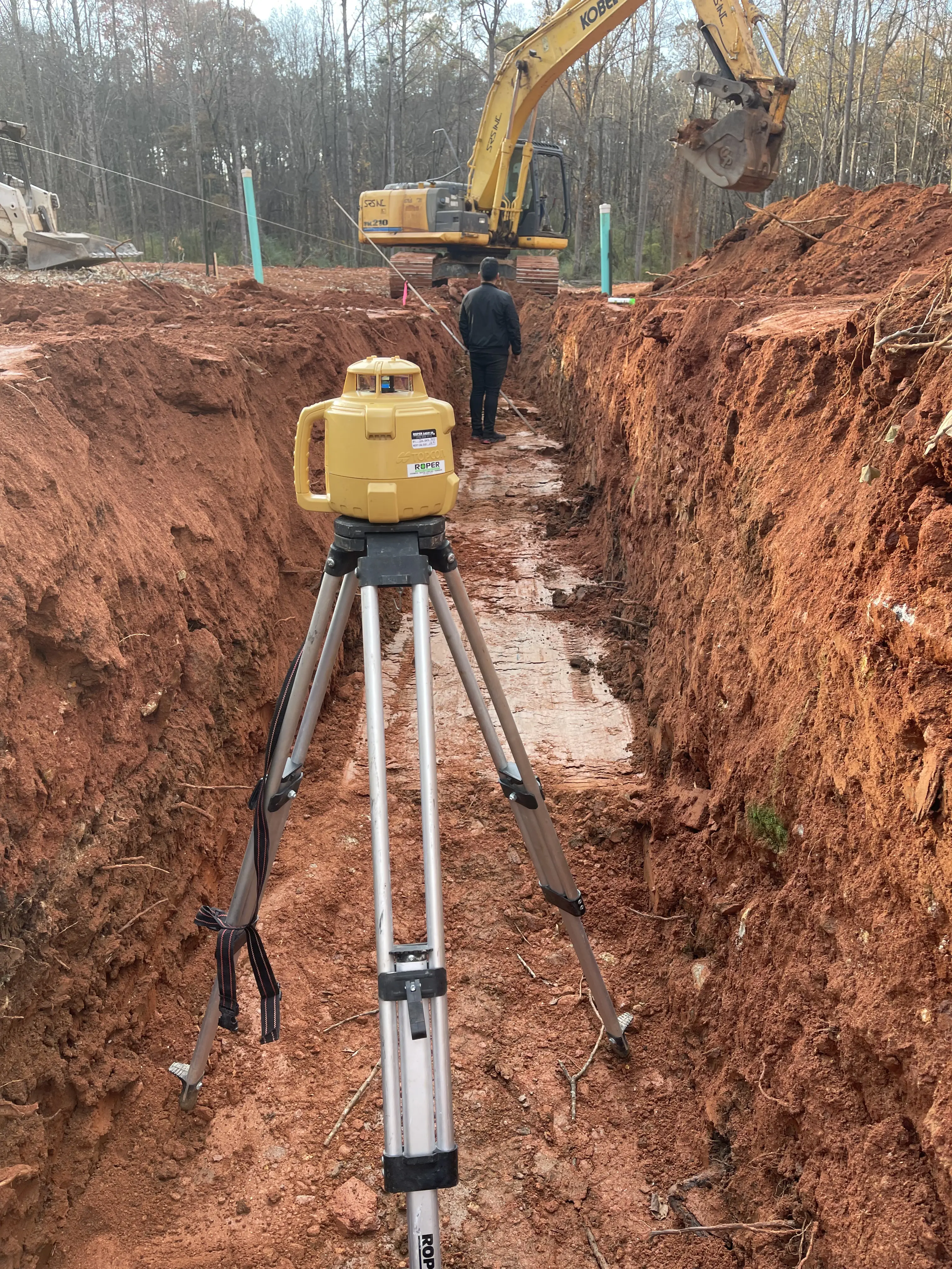 Construction site with a surveying tripod and excavator.